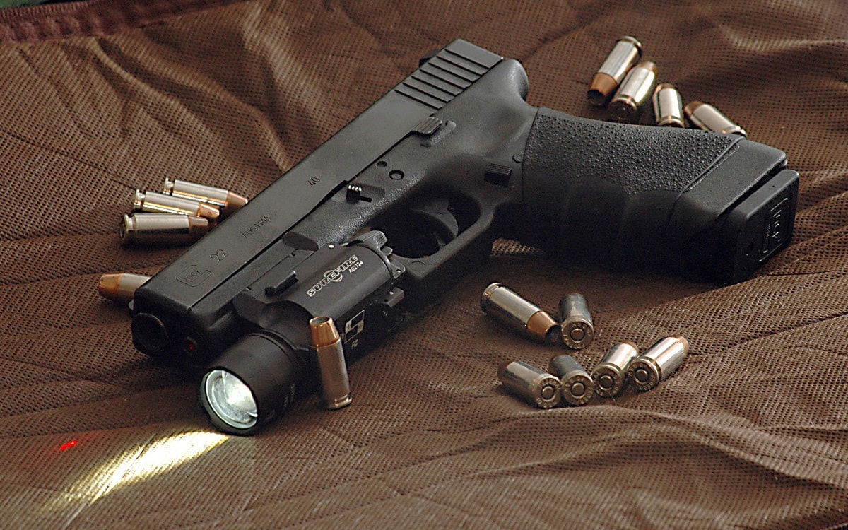 This is a Glock 22 (.40 S&W) with a few modifications. It has a Hogue rubber grip, Lasermax internal laser, extended slide takedown lever, Surefire X200a light, and Trijicon night sights. It is surrounded by .40 Hydra-shok bullets. Image: Creative Commons.