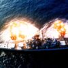 An overhead view of the battleship USS NEW JERSEY (BB-62) firing a full broadside to starboard during a main battery firing exercise. Image Credit: Creative Commons.