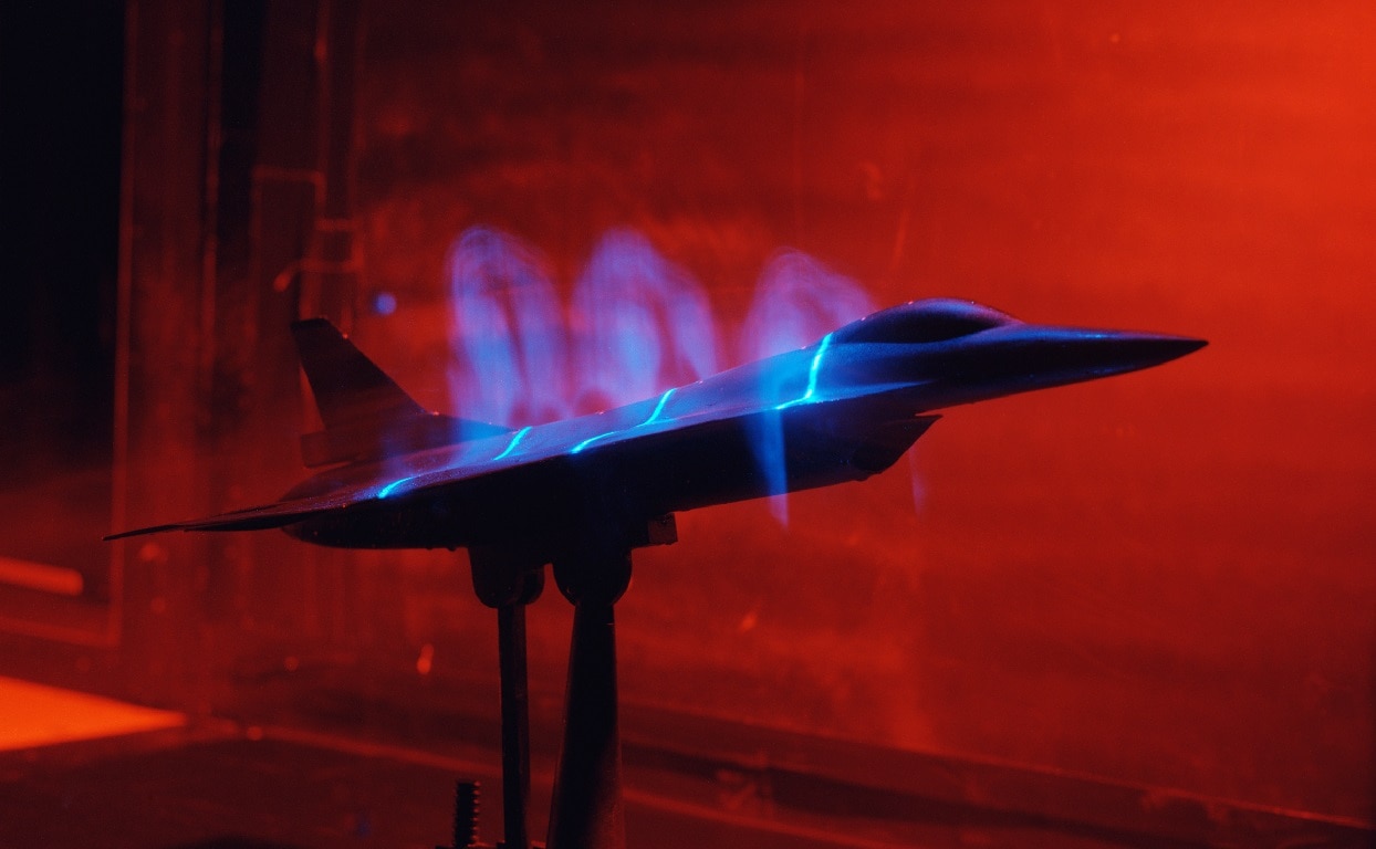 An F-16 SCAMP model at 4% scale being tested in the NASA Basic Aerodynamics Research Tunnel (Facility 1214) at the Langley Research Center. Photo shows a basic flow visualization test using smoke flowing with the air, and three laser light sheets to illuminate it above the model. This experiment highlights vortices trailing from the leading-edge and was part of the NASA High Speed Research Program. Image: Creative Commons.