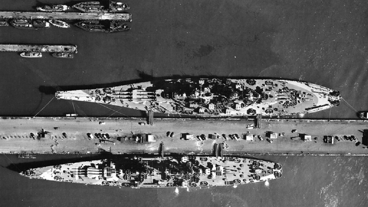 Aerial view of warships at the base piers of Norfolk Naval Base, Virginia (USA), circa August 1944. Among them are: the battleship USS Missouri (BB-63), the largest ship; the battlecruiser USS Alaska (CB-1), on the other side of the pier; the escort carrier USS Croatan (CVE-25), and two destroyers, a Fletcher-class destroyer at the pier and a Clemson/Wilkes-class-destroyer moored outboard. Image Credit: Creative Commons. 