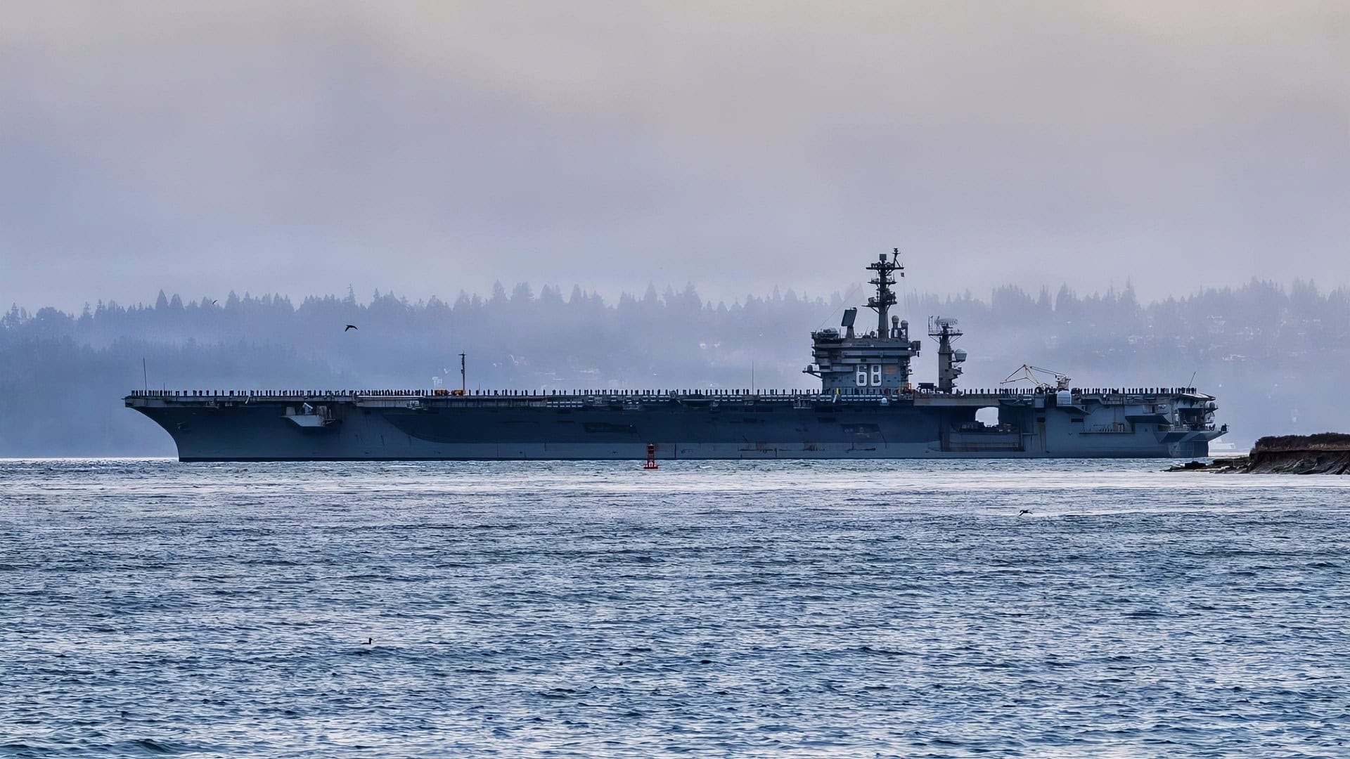 The Nimitz class aircraft carrier USS Nimitz (CVN 68) passes by a Washington State Ferry as it transits Puget Sound during the ship’s final departure from Naval Base Kitsap-Bremerton, Washington, March 7, 2026. Nimitz is underway in the U.S. 3rd Fleet area of operations as part of a scheduled homeport shift to Norfolk, Virginia. (U.S. Navy photo by Mass Communication Specialist Seaman Kimberli Ibarra Ruiz)