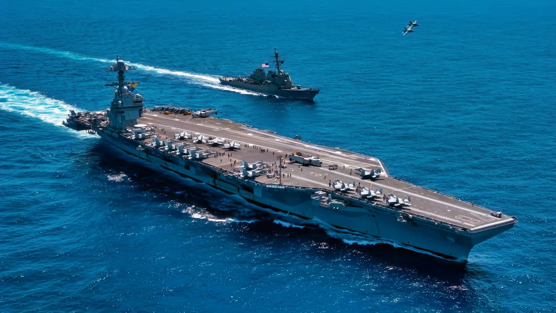 An F/A-18F Super Hornet, attached to the "Blacklions" of Strike Fighter Squadron (VFA) 213 and a F/A-18E Super Hornet, attached to the "Golden Warriors" of Strike Fighter Squadron (VFA) 87 fly over the world's largest aircraft carrier, USS Gerald R. Ford (CVN 78), the Arleigh Burke-class guided-missile destroyer USS Mahan (DDG 72), April 11, 2025. The Gerald R. Ford Carrier Strike Group is underway in the Atlantic Ocean completing integrated naval warfighting training. Composite Training Unit Exercise (COMPTUEX) is the Joint Force’s most complex integrated training event and prepares naval task forces for sustained high-end Joint and combined combat. Integrated naval training provides America’s civilian leaders and commanders highly-capable forces that deter adversaries, underpin American security and economic prosperity, and reassure Allies and partners. (U.S. Navy photo by Mass Communication Specialist 2nd Class Maxwell Orlosky