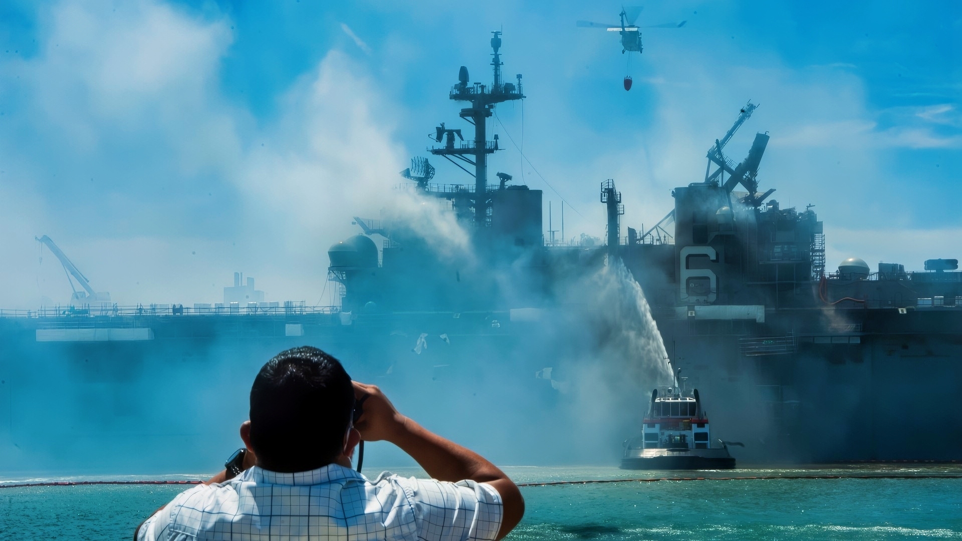 SAN DIEGO (July 13, 2020) An MH-60S Seahawk helicopter from the “Merlins” of Helicopter Sea Combat Squadron (HSC) 3, provides aerial firefighting support alongside Sailors and civilian fire crews on the ground to fight the fire aboard amphibious assault ship USS Bonhomme Richard (LHD 6). On the morning of July 12, a fire was called away aboard the ship while it was moored pier side at Naval Base San Diego. Base and shipboard firefighters responded to the fire. Bonhomme Richard is going through a maintenance availability, which began in 2018. (U.S. Navy photo by Mass Communication Specialist 3rd Class Mar'Queon A. D. Tramble)